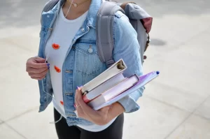 Female student wearing a jean jacket and a backpack carrying text books in her left hand as she walks to her concurrent enrollment class.