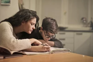 a homeschooling mother reading over a book with her child at a brown table