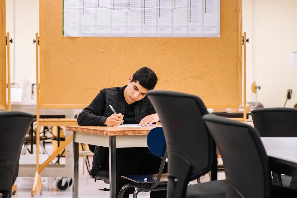 Male student sitting at a desk in a classroom taking a AP high school class