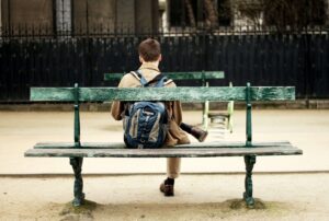 college student wearing a backpack sitting on a bench alone