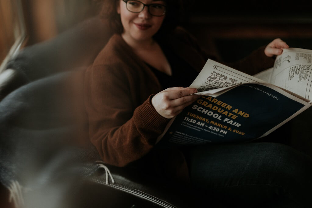 female college student sitting in a chair reading a magazine about career and graduate school