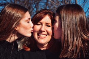 two daughters kissing the cheeks of their mother showing appreciation that she helped them get scholarships for college