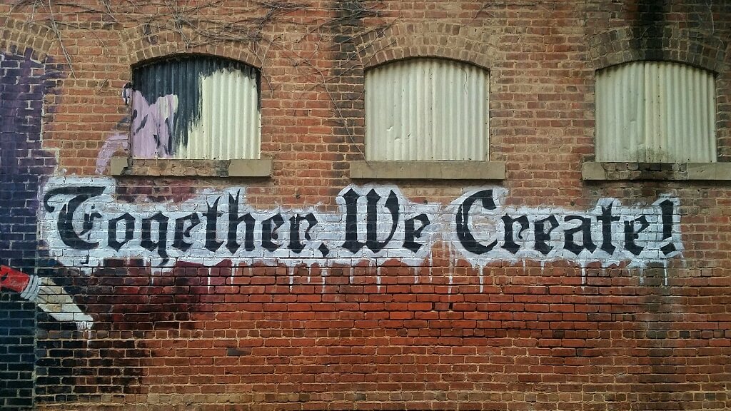 the words "Together we create" spray painted on a brick wall representing the inclusivity of the Golisano Institute