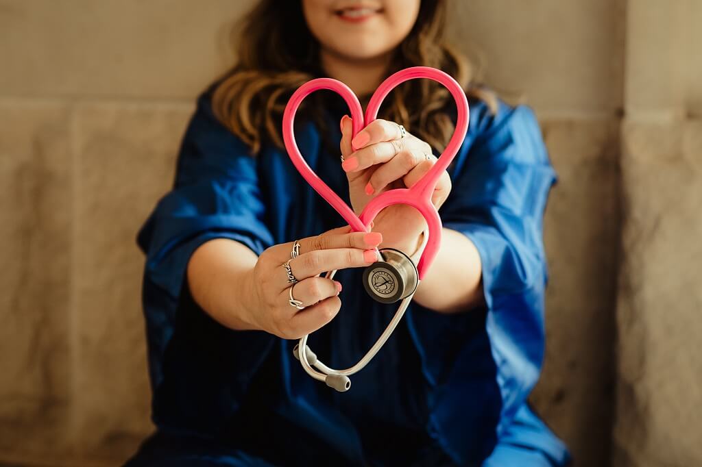 college female nurse degree student sitting with pink stethoscope shaped into a heart.